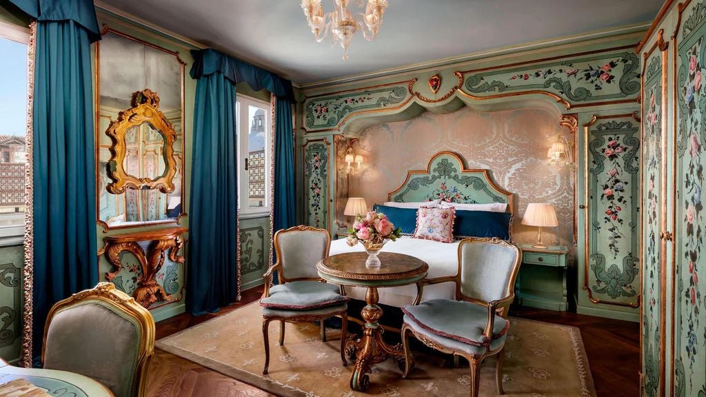 Opulent Venetian hotel room with gold-framed mirrors, crystal chandelier, antique furniture and panoramic views of the Grand Canal