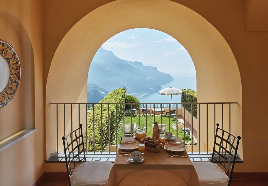 Infinity pool overlooking Amalfi Coast cliffs and Mediterranean Sea at sunset, with elegant stone terraces and manicured gardens below