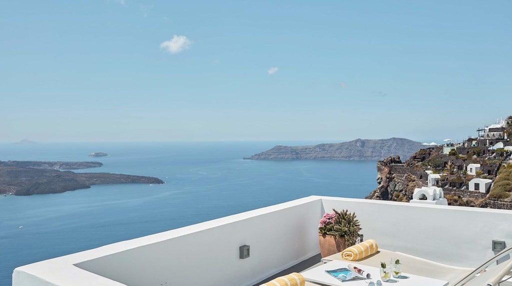 Luxurious white-walled Santorini suite with private jetted tub, panoramic Aegean Sea view, minimalist design, and elegant honeymoon ambiance