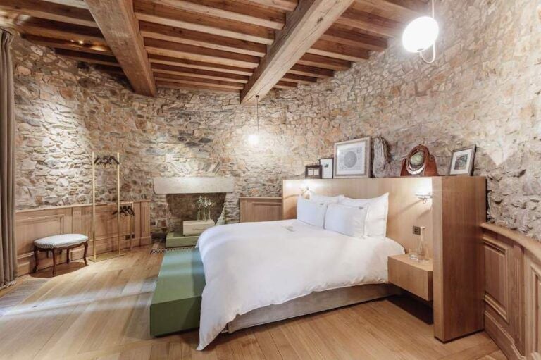 Elegant French luxury hotel room with soft neutral tones, modern minimalist design, plush bedding, and expansive windows overlooking scenic countryside landscape