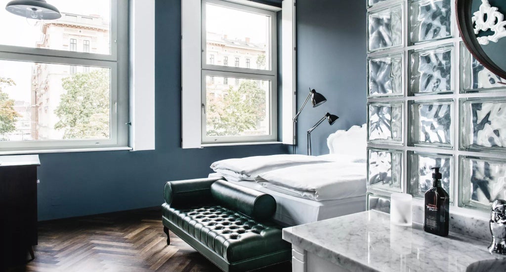 Elegant Austrian hotel room with plush white bedding, wooden floors, large windows overlooking cityscape, and sophisticated minimalist design highlighting luxury accommodations.