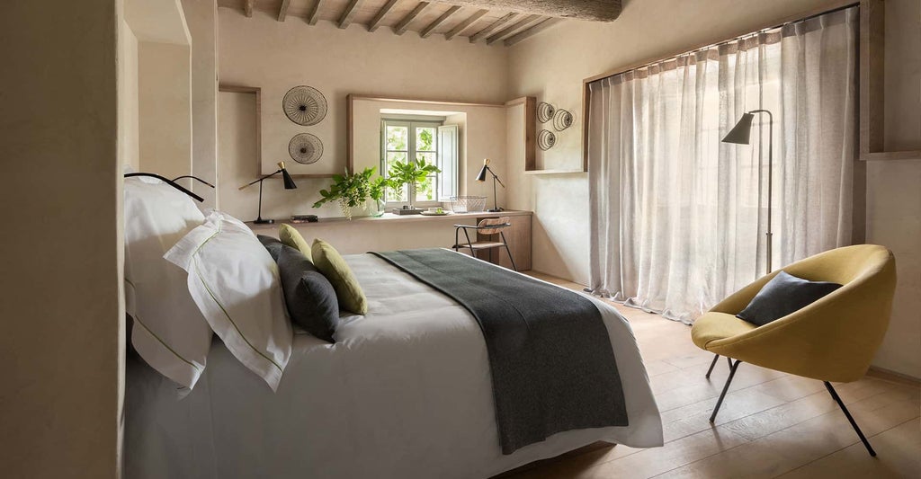 Elegant junior suite at Scenset's Badia di Pomaio, featuring rustic Tuscan decor, plush bed, and warm natural light streaming through arched windows