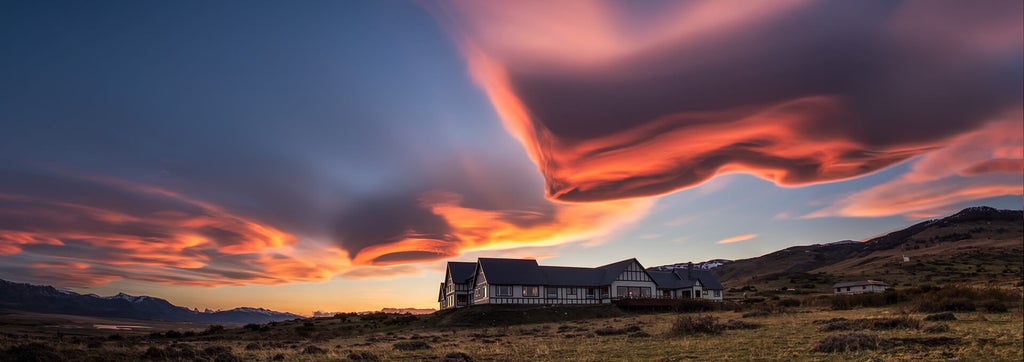 Remote luxury lodge with floor-to-ceiling windows nestled in Patagonian plains, snow-capped mountains in background at golden hour