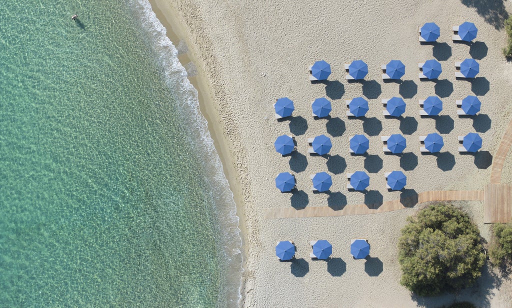 Whitewashed luxury hotel with curved architecture overlooking the Aegean Sea, featuring infinity pools and private terraces at sunset