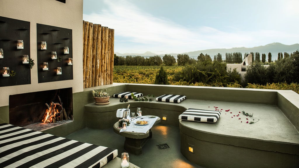 Elegant stone villa nestled in Mendoza vineyards with snow-capped Andes mountains in background, luxury pool reflecting sunset sky