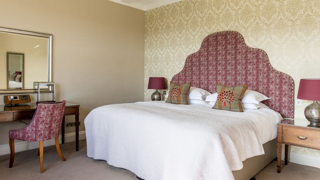 Elegant valley-view hotel room at Bovey Castle, featuring plush bedding, traditional decor, and expansive windows overlooking lush countryside landscape.