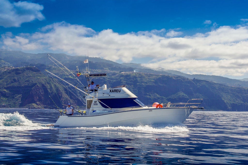 Luxury deep sea fishing boat off scenic Madeira coastline, skilled anglers casting lines into crystal-blue Atlantic waters with rugged cliffs backdrop