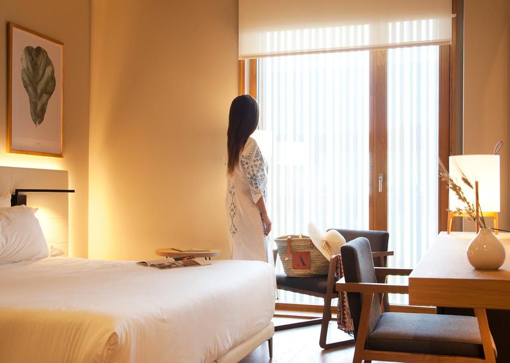 Elegant minimalist hotel room with neutral color palette, large window, modern furnishings, and subtle spa-inspired design in Spanish architectural style