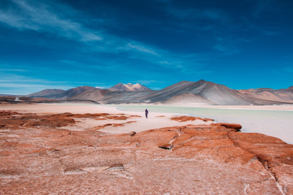 Vibrant sunset illuminates red rock formations in Chile's Atacama Desert, casting golden light across rugged peaks and vast sandy plains