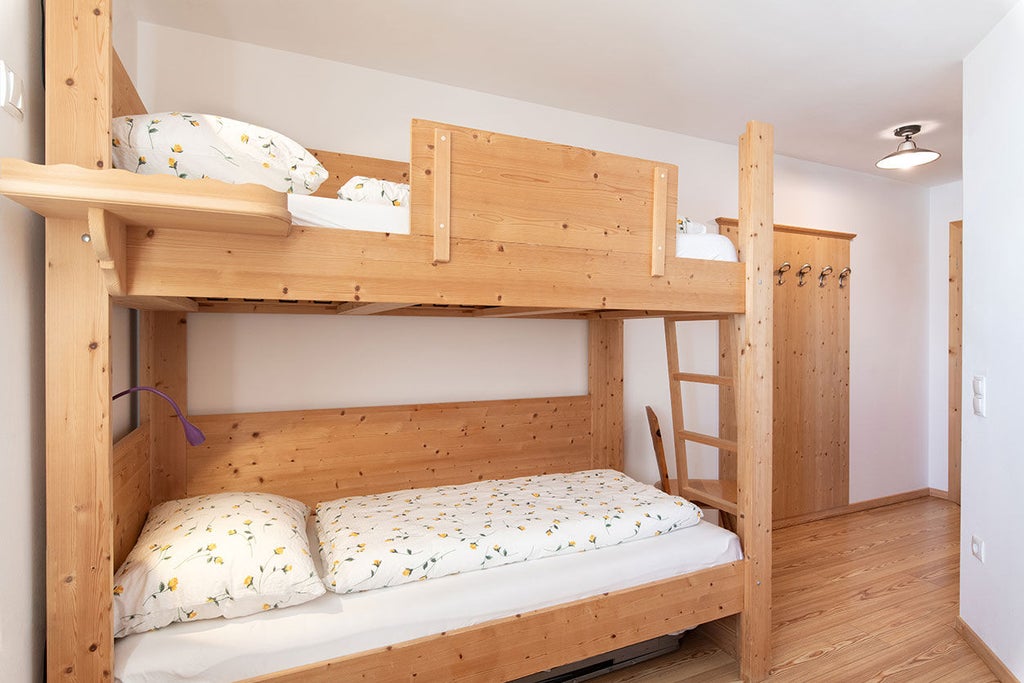 Cozy mountain lodge room featuring rustic wooden bunk beds, private modern bathroom, and panoramic window with stunning Dolomite views