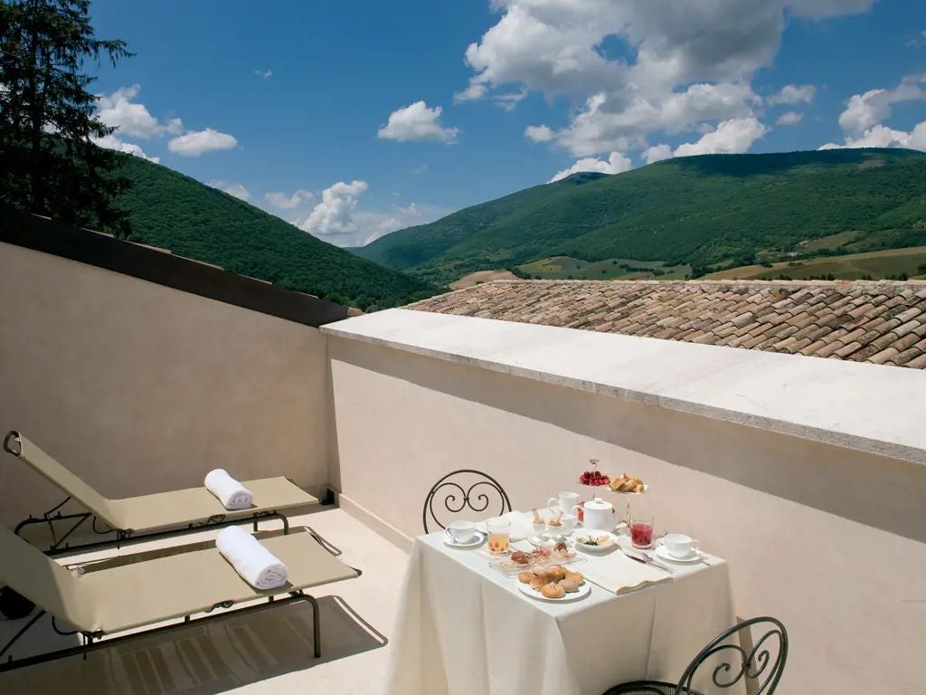 Elegant stone facade of historic Palazzo Seneca hotel in Norcia, showcasing refined Italian Renaissance architecture with warm limestone walls at sunset