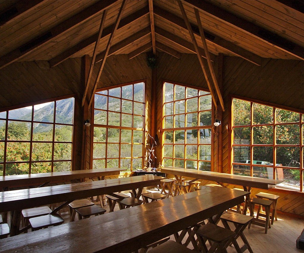 Spacious mountain-view hostel room with wooden furnishings, cozy bed, and large windows overlooking scenic Patagonian landscape in Chile