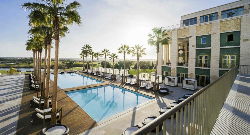 Elegant Mediterranean-style luxury hotel with palm-lined infinity pool overlooking manicured gardens and Algarve golf course at sunset