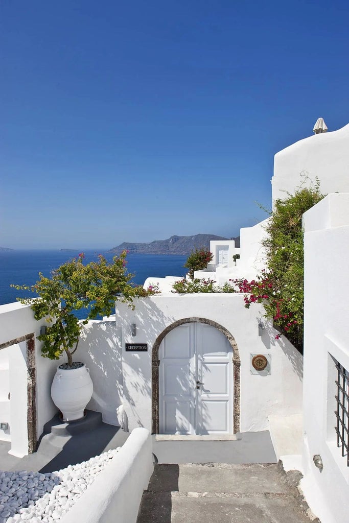 Luxurious white-washed Greek hotel suite with private infinity pool overlooking Santorini's caldera and Aegean Sea at sunset