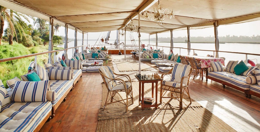 Traditional wooden dahabiya boat with elegant red sails cruising the Nile, featuring ornate Arabic designs and luxurious deck seating at sunset