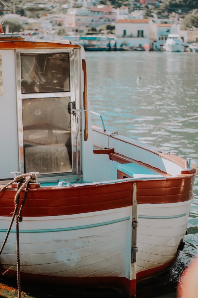 Traditional wooden fishing boat gliding across turquoise Mediterranean waters near Taormina, with Mount Etna's peak in the background