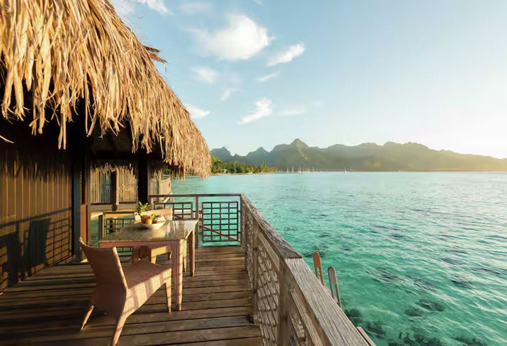 Luxurious overwater bungalow with glass floor panel, king bed, and panoramic windows overlooking turquoise Moorea lagoon