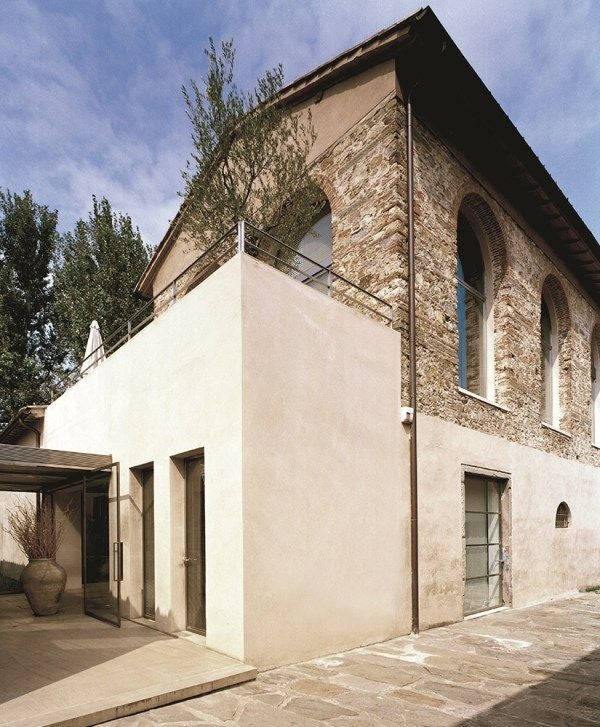 Elegant Tuscan-style loft with rustic wooden beams, minimalist decor, and large windows overlooking Florence's scenic landscape at sunset