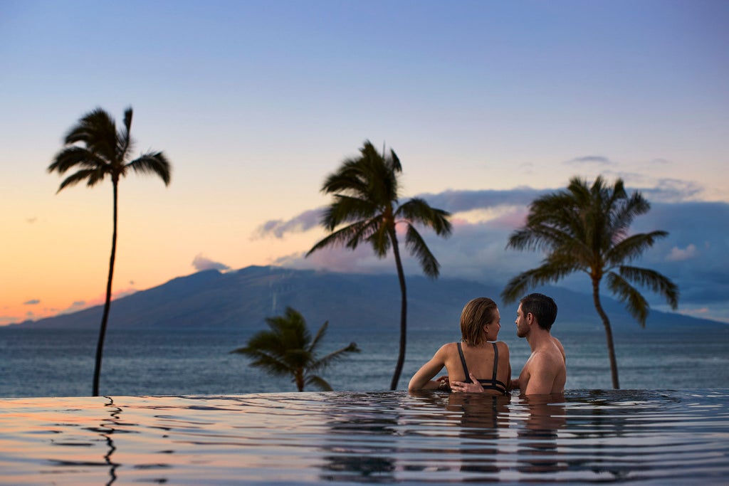 Luxurious oceanfront Four Seasons resort in Maui with infinity pool overlooking Pacific Ocean, swaying palm trees and sunset-lit mountains