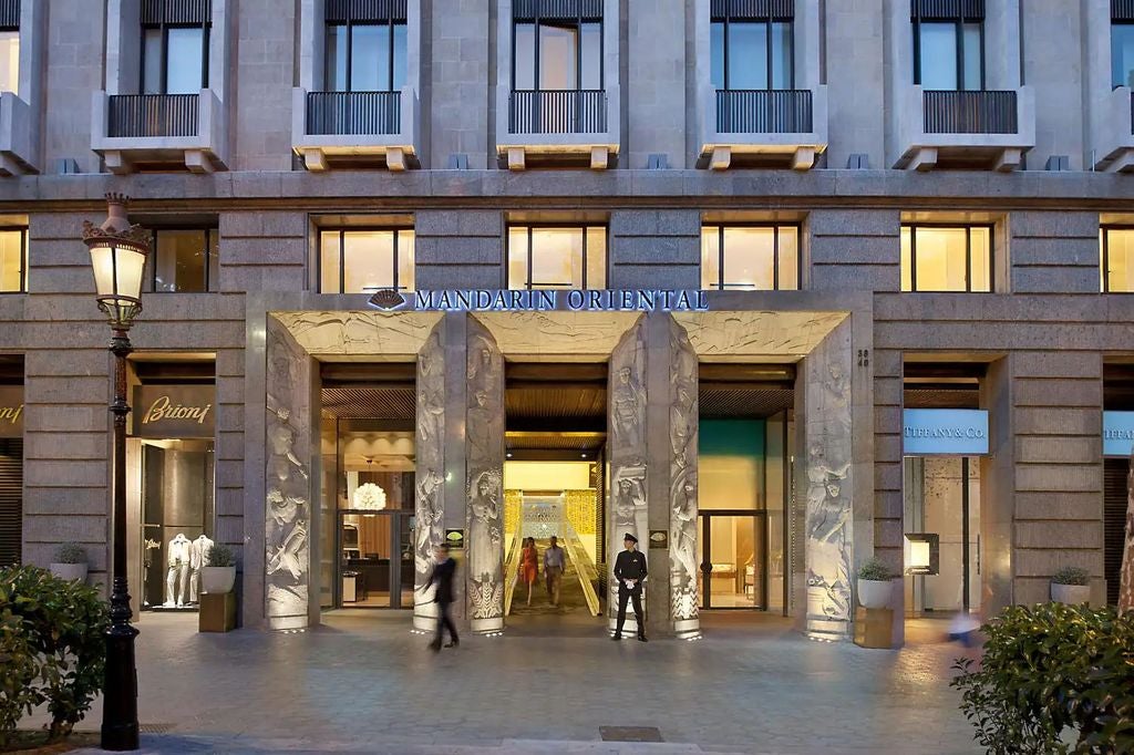 Contemporary luxury hotel facade with sleek glass windows, elegant stone columns and landscaped entrance on Barcelona's Passeig de Gràcia