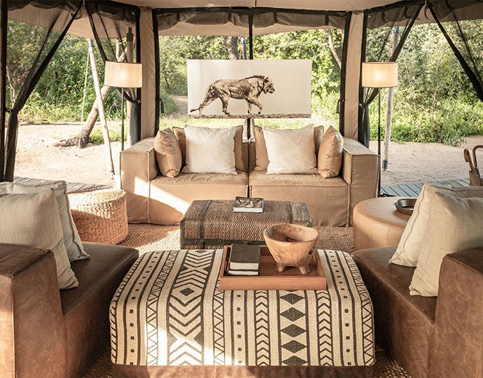 Elevated luxury tented camp overlooking Tanzania's savanna, with canvas suite perched on wooden deck amid acacia trees at golden hour