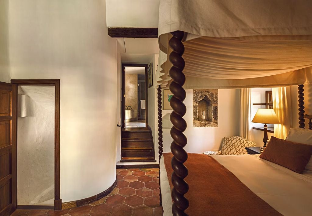 Elegant Tower Suite bedroom with draped four-poster bed, stone walls, antique furniture, and stunning mountain views through arched windows