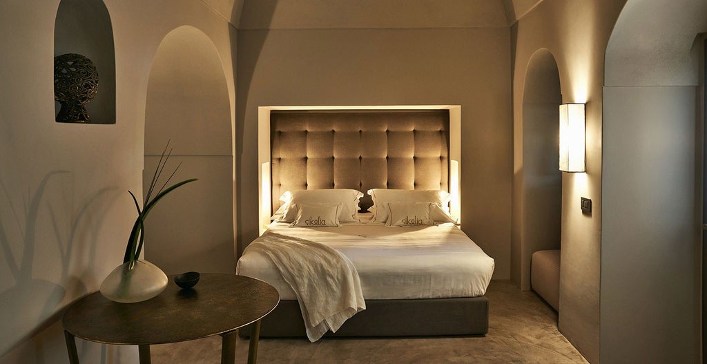 Luxurious Pantesche Suite at Sikelia, with minimalist white decor, elegant bed, and soft natural light illuminating the serene Mediterranean-inspired space