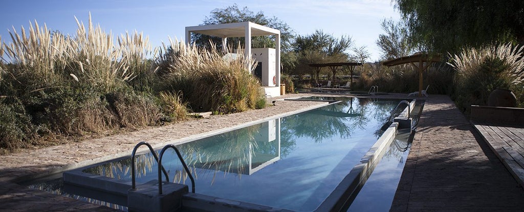 Modern desert resort with tan stone walls and thatched roofs nestled against Atacama mountains under a bright blue Chilean sky