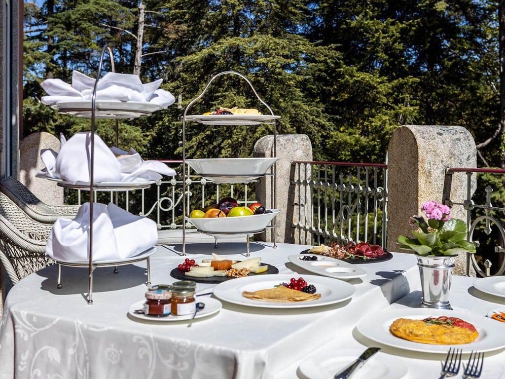 Elegant junior suite at Vidago Palace Hotel with plush white bedding, ornate furnishings, large windows overlooking Portuguese landscape, blending classic luxury and modern comfort