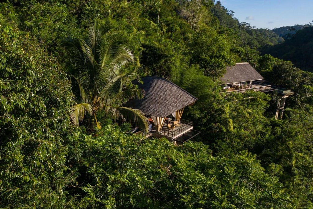 Elegant open-air jungle villa with infinity pool overlooking lush Balinese rainforest, featuring thatched roof and natural materials