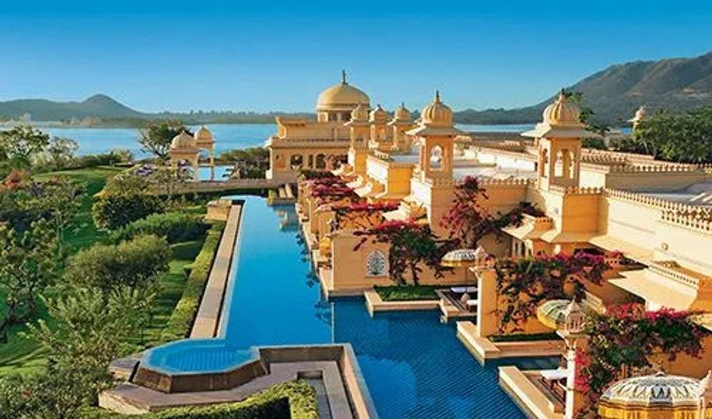 Grand domed palace hotel with ornate Rajasthani architecture, reflecting in serene waters amid manicured gardens at golden sunset