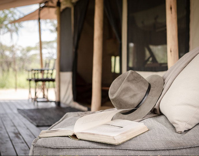 Upscale safari tent overlooking vast African savanna at sunset, featuring private wooden deck, canvas walls and panoramic mountain views