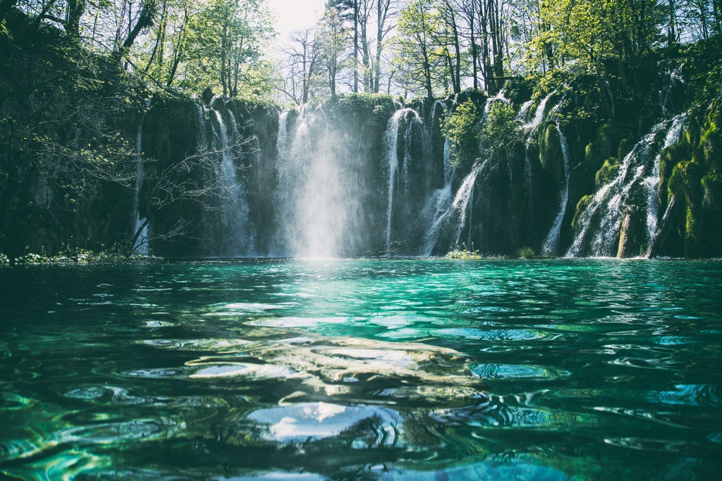 Tranquil wooden pathway meanders through turquoise lakes and cascading waterfalls in Croatia's pristine Plitvice Lakes paradise