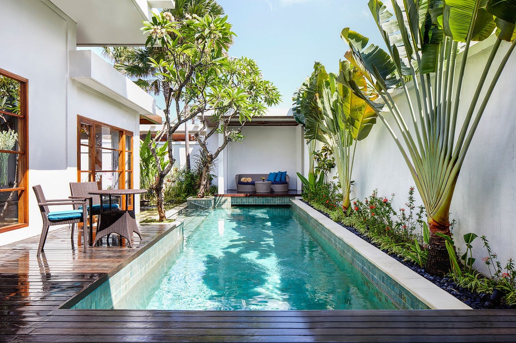 Private infinity pool overlooking lush tropical gardens at luxury Balinese resort, with contemporary villa and traditional architecture