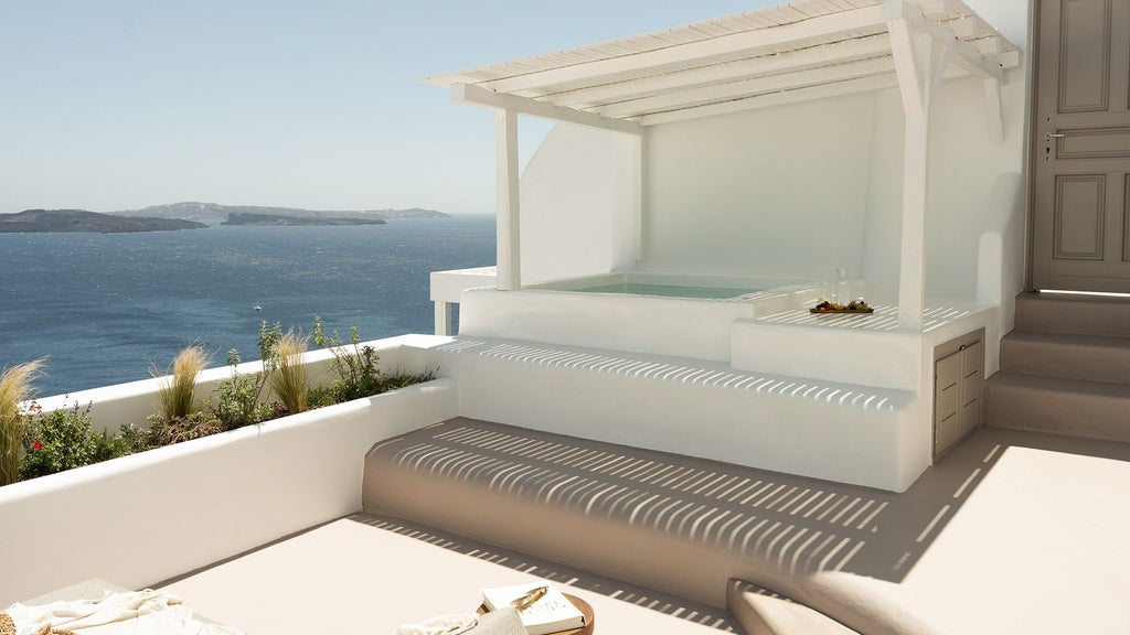 Luxurious white minimalist honeymoon suite with infinity pool overlooking Oia's iconic blue-domed churches and Aegean Sea in Santorini, Greece