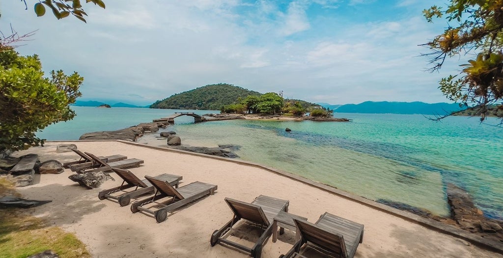 Five-star oceanfront resort with infinity pool overlooking Angra Bay, featuring modern architecture and palm-lined terraces at sunset