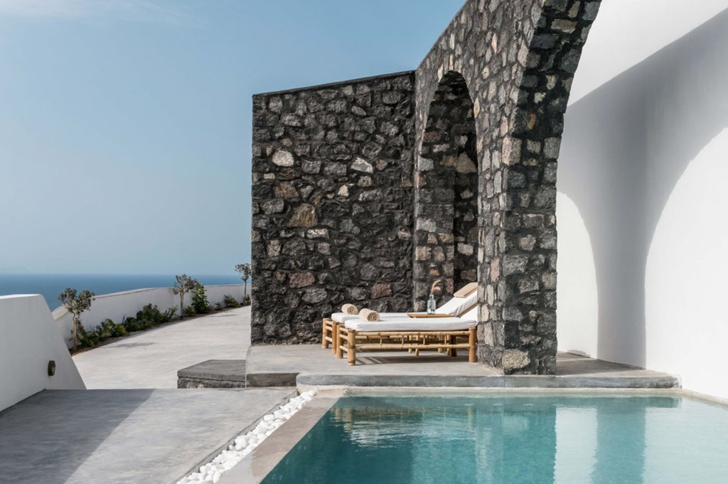 Luxury white cliffside suites with private infinity pools overlooking the Aegean Sea and Santorini caldera at sunset