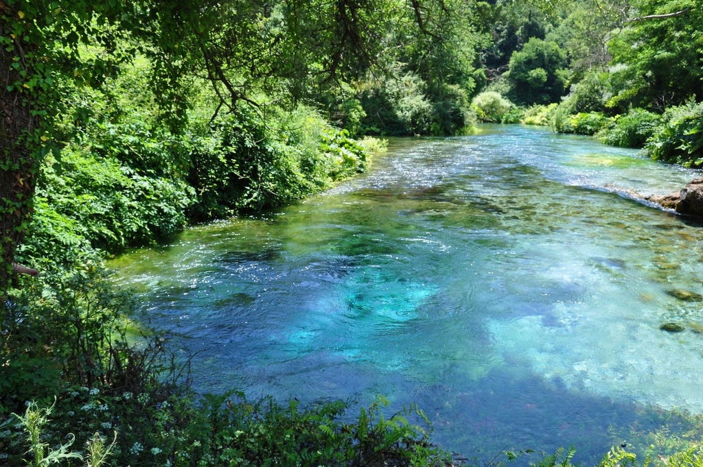 Blue Eye Spring's crystal-clear turquoise waters cascade through limestone, framed by lush Albanian wilderness with an elegant culinary setup nearby