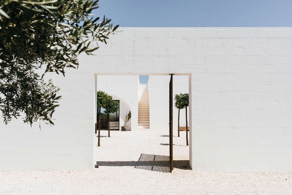 Whitewashed Mediterranean villa with stone walls, surrounded by olive groves, showcasing minimalist luxury against the backdrop of scenic Italian countryside