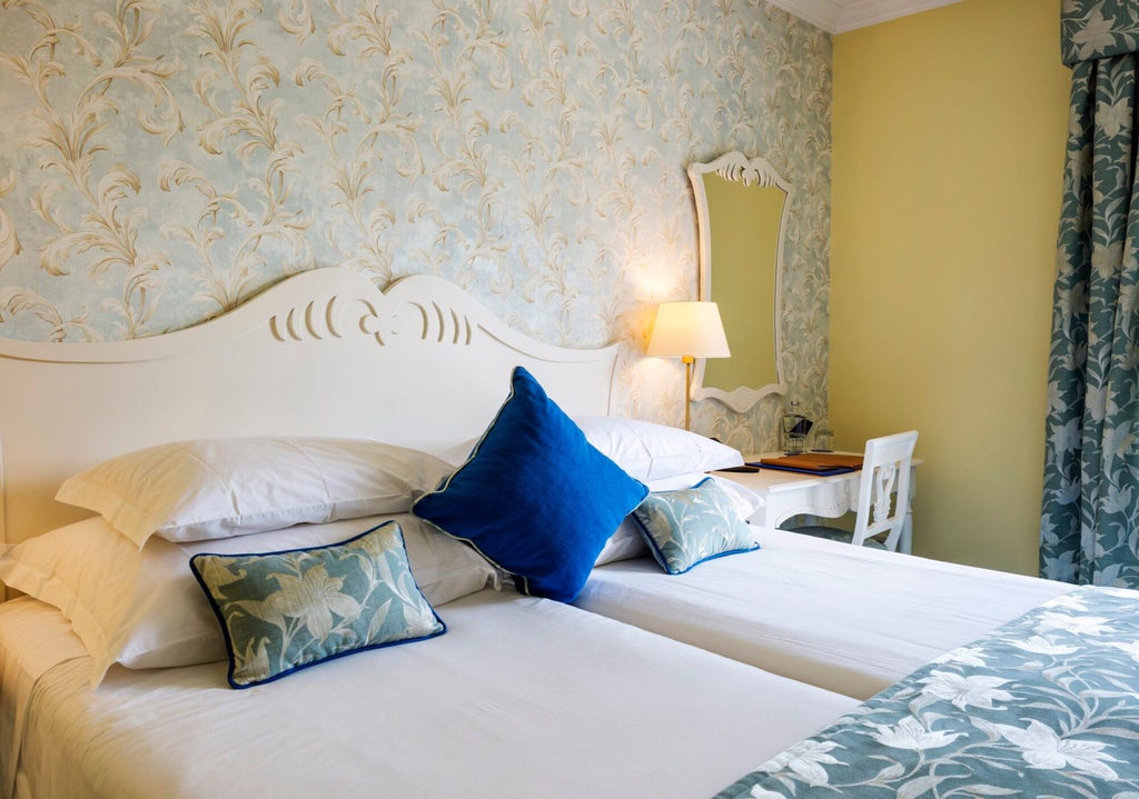 Elegant standard room with vintage wooden furnishings, soft neutral palette, plush bedding, and large windows overlooking traditional Portuguese architectural landscape