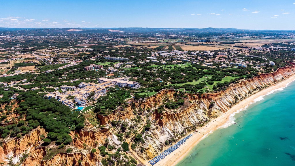 Elegant coastal resort with whitewashed Mediterranean buildings nestled among pine trees overlooking azure Algarve cliffs and sea