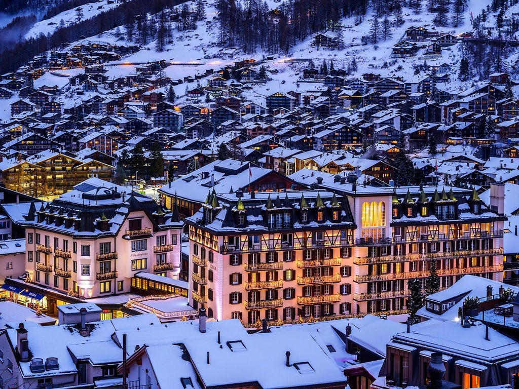 Majestic five-star alpine hotel Mont Cervin Palace with wooden balconies and Swiss flags against snow-capped mountains in Zermatt