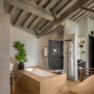 Elegant Italian junior suite with rustic wooden floors, plush white bedding, and panoramic countryside views of rolling Tuscan hills through large windows