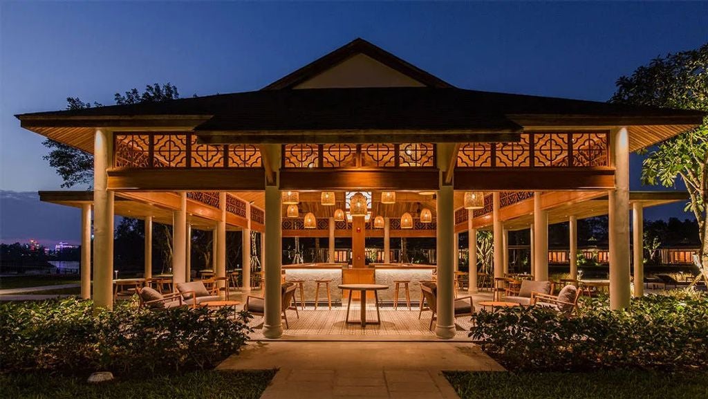 Modern luxury resort pavilions with overwater walkways surrounded by lush tropical gardens along Mekong Delta waterways at sunset