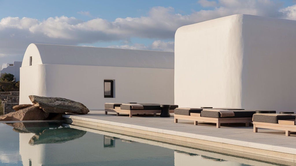 Whitewashed luxury resort in Mykonos with private infinity pools overlooking the Aegean Sea, set against a mountainous backdrop