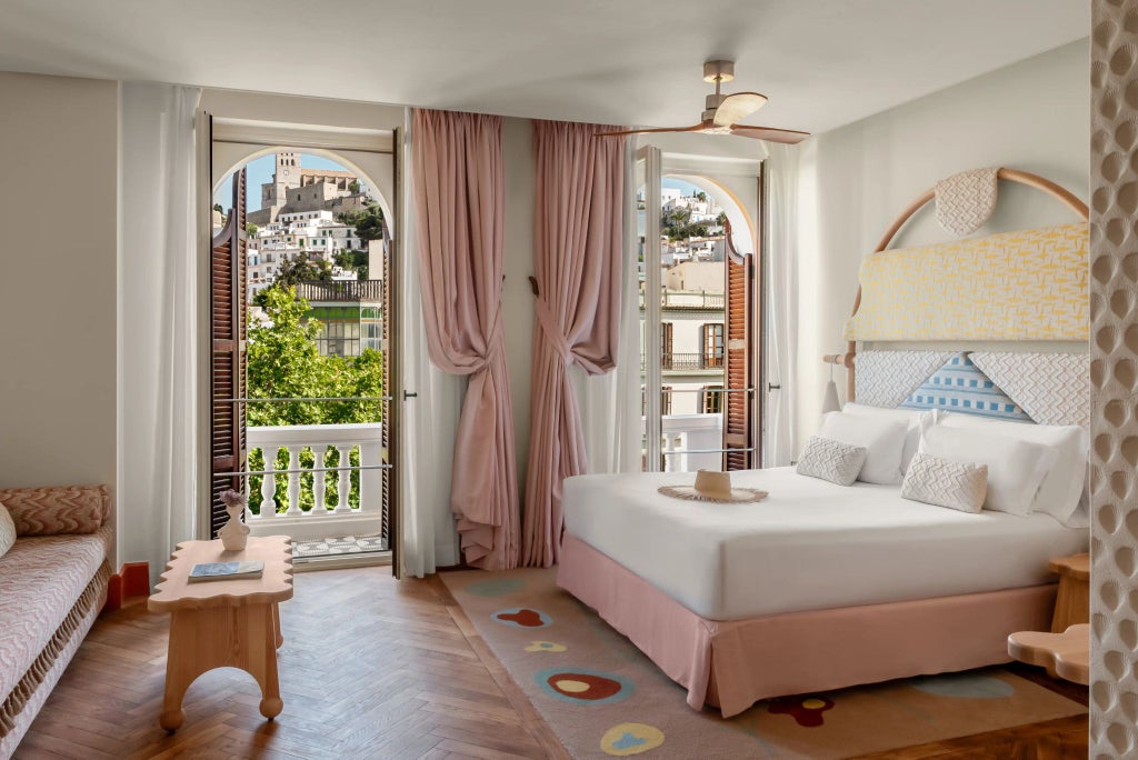 Minimalist white hotel room with sleek furniture, large windows overlooking Ibiza's urban landscape, elegant design blending contemporary style with Mediterranean charm