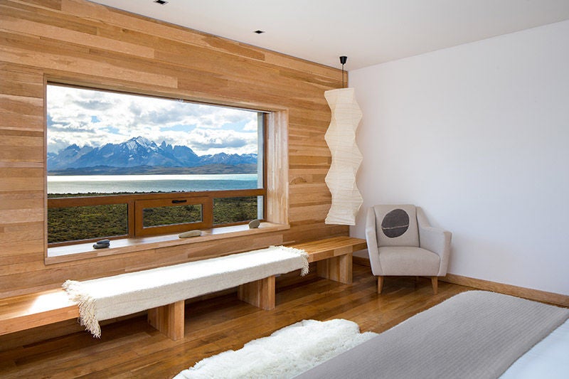 Modern luxury hotel with curved wooden architecture nestled in Torres del Paine mountains, reflecting in a lake at golden hour