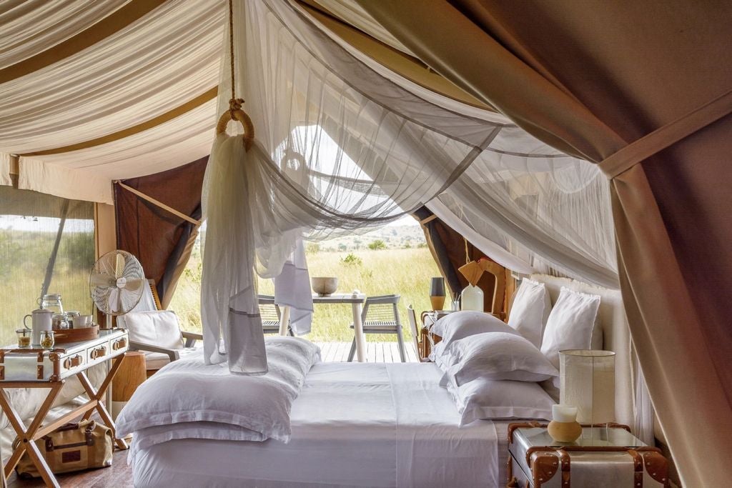 Luxurious safari tent at dusk overlooking Mara River, with canvas walls, private deck, and atmospheric lantern lighting in Tanzania