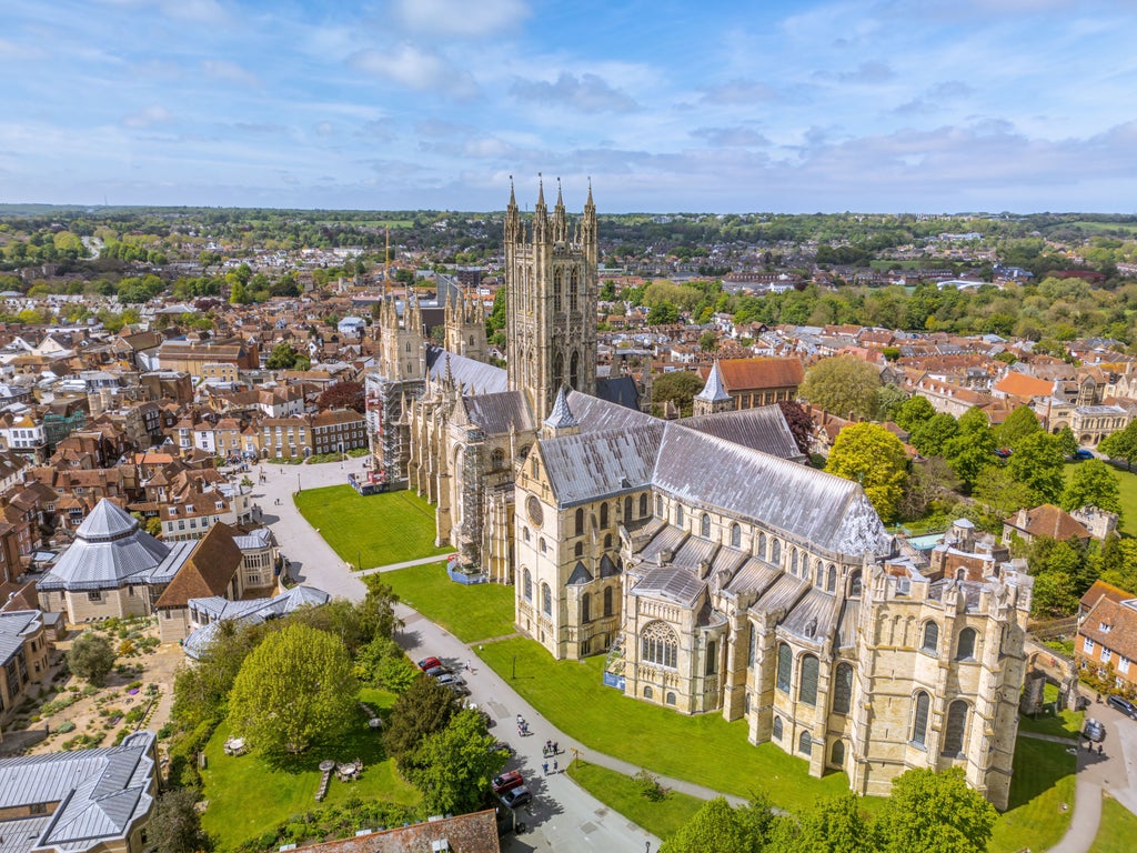 Historic Canterbury Cathedral spires rise above medieval city buildings, with cobblestone streets and traditional Tudor-style architecture