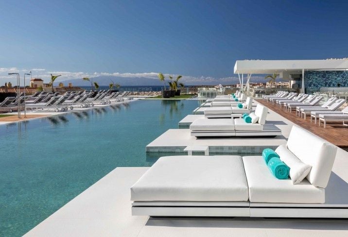 Modern white resort building with curved balconies and infinity pools overlooking the Atlantic Ocean, set against Tenerife's coastline